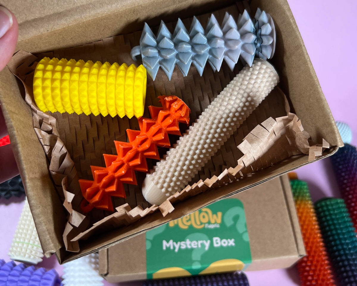 Mellow Fidgets Pain Stim Mystery Box containing four random 3D printed spiky sensory fidget toys in assorted colours and textures.